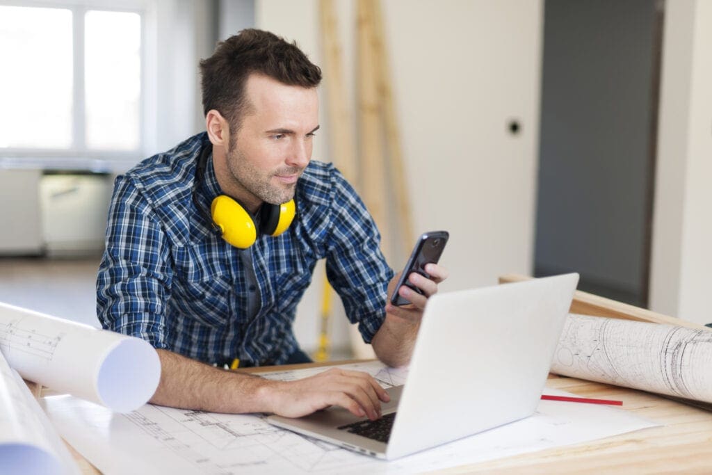Construction worker using a laptop and phone.
