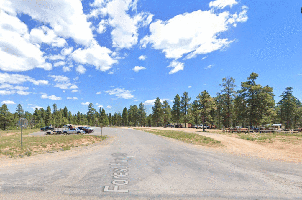 Rural road intersection with trees and cars.